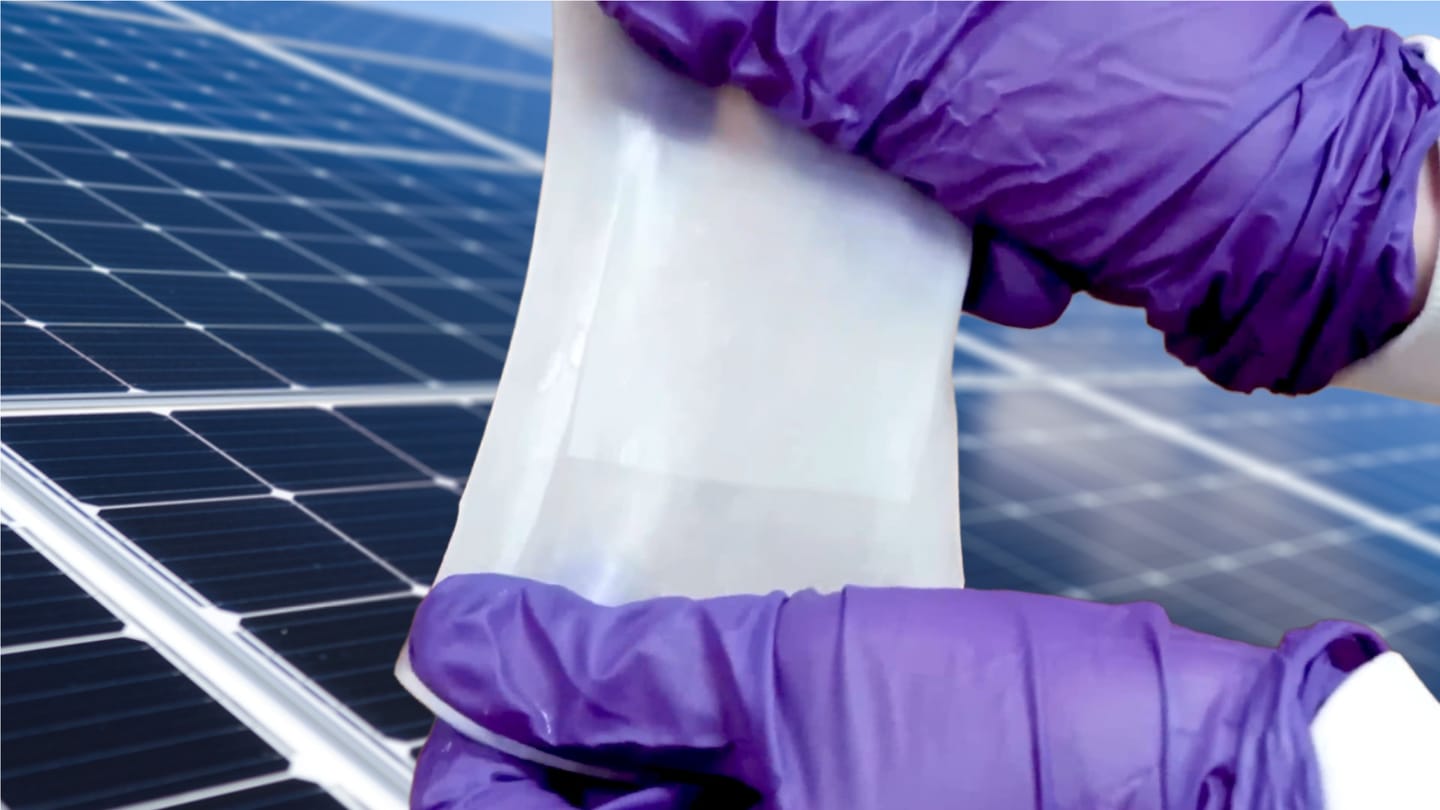 A pair of gloved hands stretching hydrogel in front of solar panels