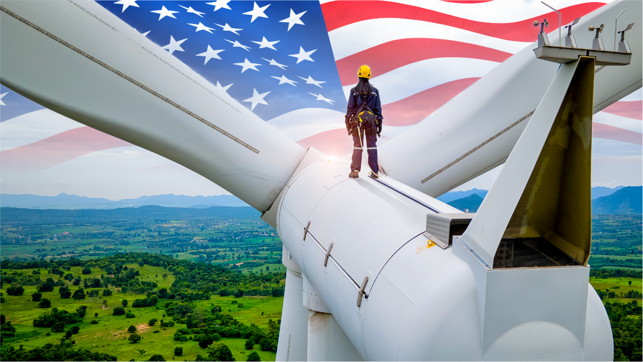 A figure stood atop a wind turbine, looking over a wooded area, with the American flag imposed over the sky