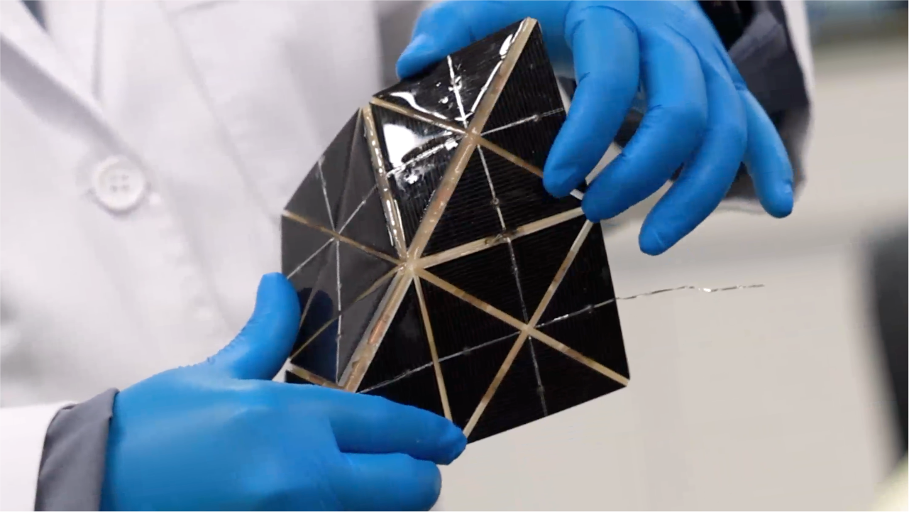 A pair of blue-gloved hands holding a 3d shifting solar panel